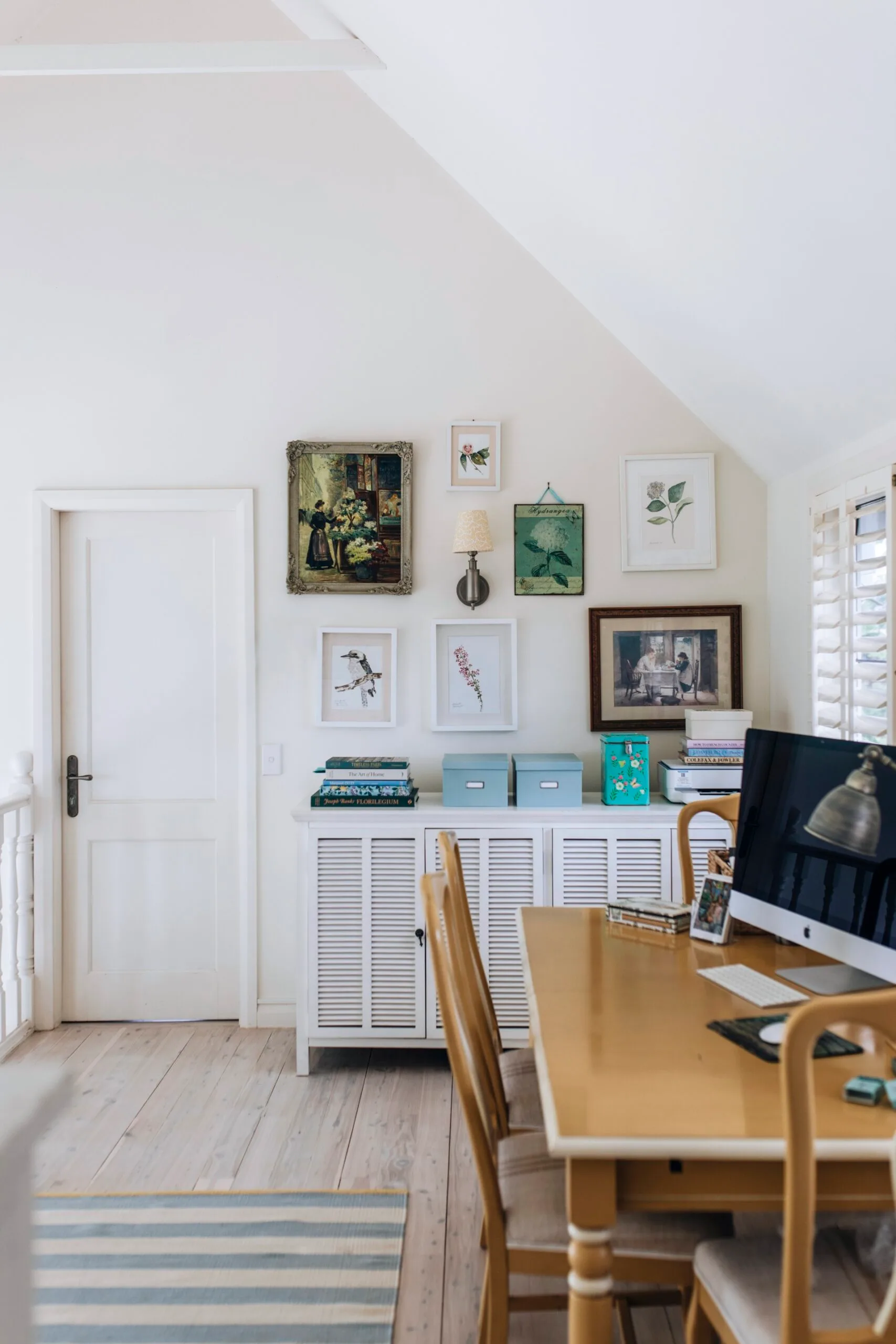 A wooden desk with art on the wall in the study of a Nantucket inspired home. 