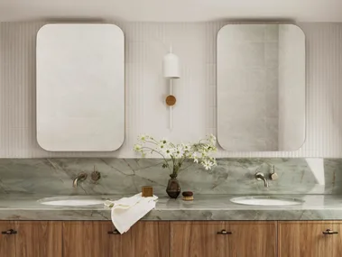 A bathroom vanity with timber cupboards, sage green stone benchtop and splashback, two rectangular mirrors and white wall tiles. A skylight is above.