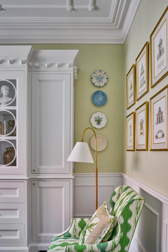 A study with green walls, white cabinetry and artwork on the walls.