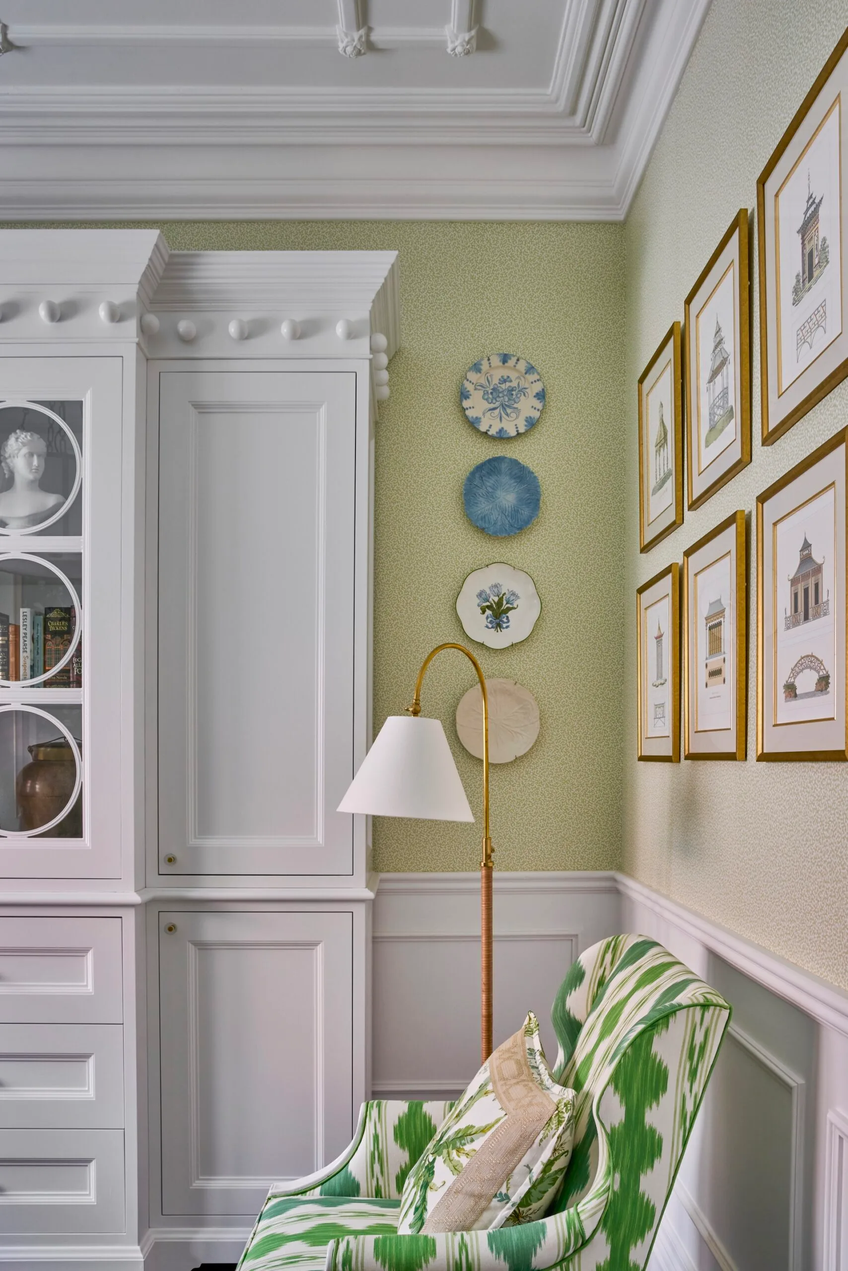 A study with green walls, white cabinetry and artwork on the walls. 