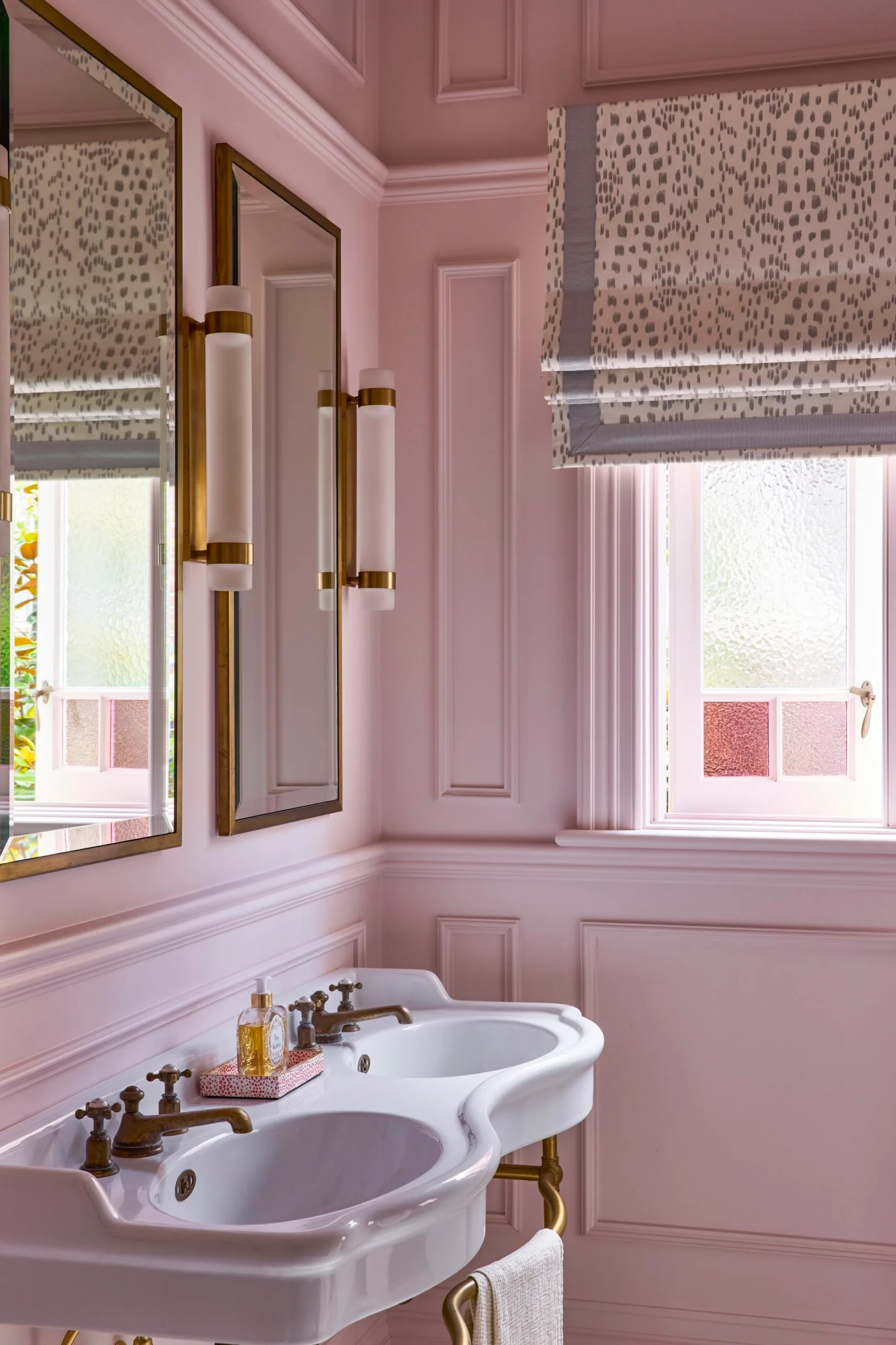 A pink bathroom with pink patterned roman blinds. 