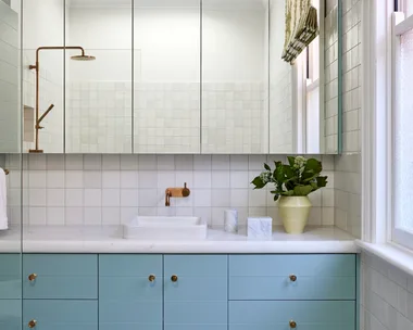 A bathroom in a Federation home with green and white tessellated tiles, teal joinery, a white benchtop and mirror.