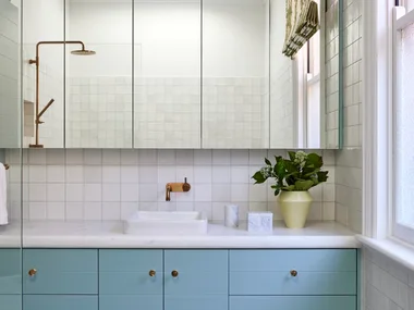 A bathroom in a Federation home with green and white tessellated tiles, teal joinery, a white benchtop and mirror.