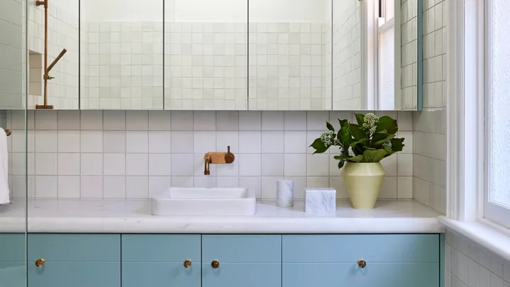 A bathroom in a Federation home with green and white tessellated tiles, teal joinery, a white benchtop and mirror.
