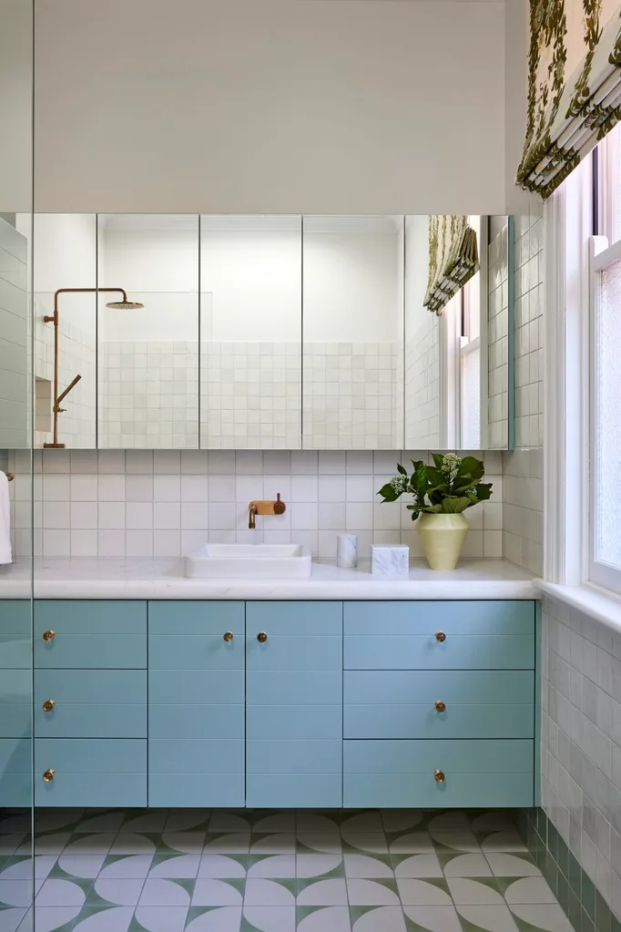 A bathroom in a Federation home with green and white tessellated tiles, teal joinery, a white benchtop and mirror.