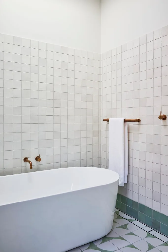 A bathroom in a Federation home with green and white tessellated tiles on the floor, a white freestanding bathtub and brass tapware.