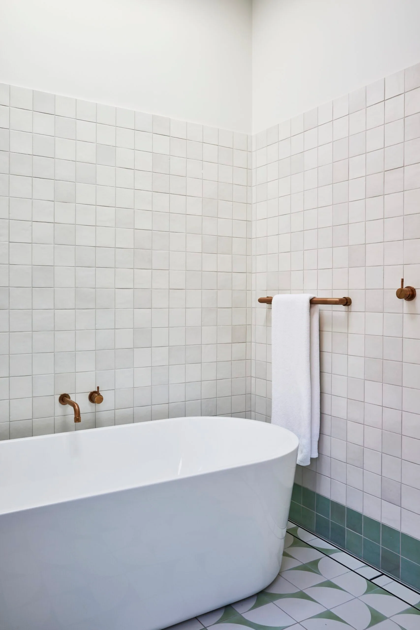 A bathroom in a Federation home with green and white tessellated tiles on the floor, a white freestanding bathtub and brass tapware.
