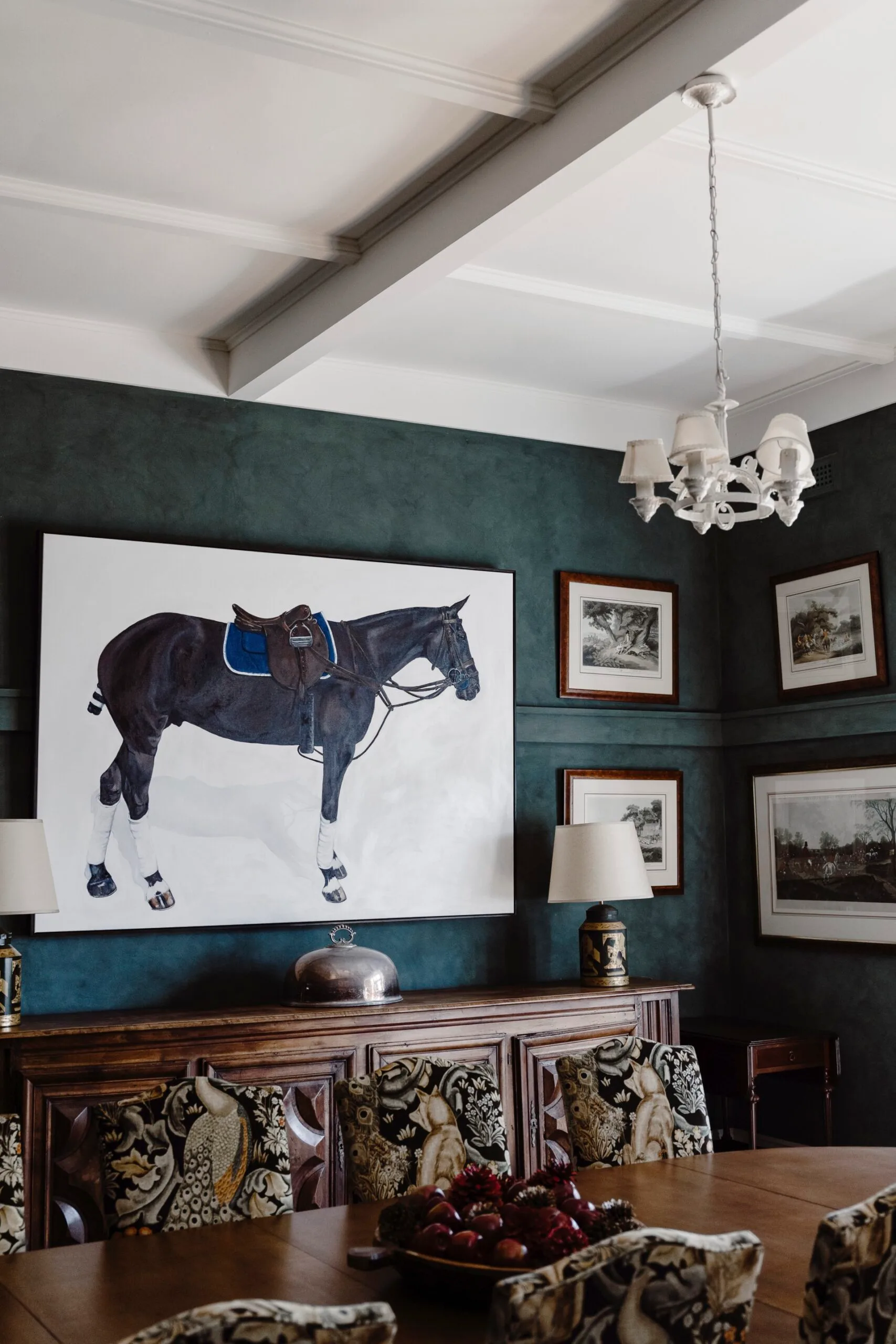 A deep green painted wall with a horse artwork in a formal dining room. 