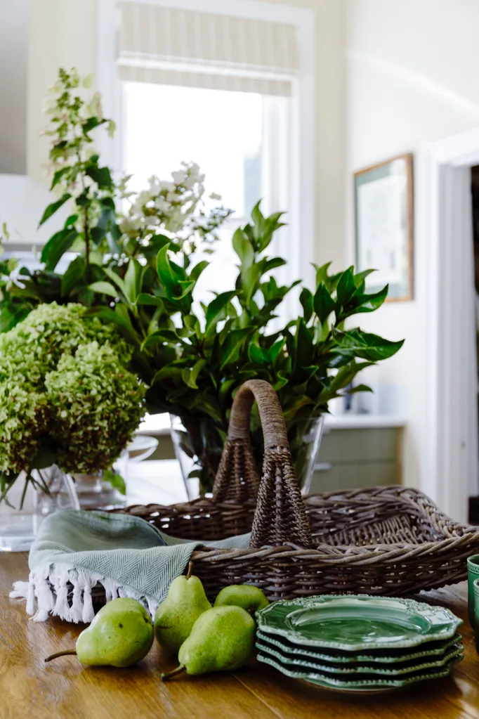 A kitchen table filled with plates, flowers and a wicker basket.