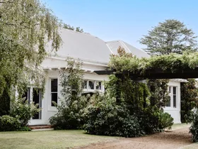 The exterior of a white homestead with lush greenery.