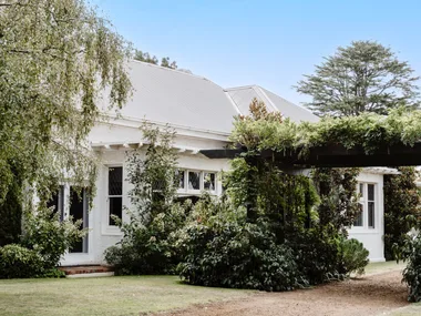 The exterior of a white homestead with lush greenery.