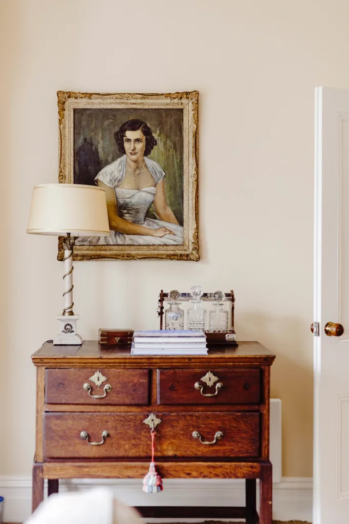 A vintage chest of drawers topped with a lamp and an artwork.