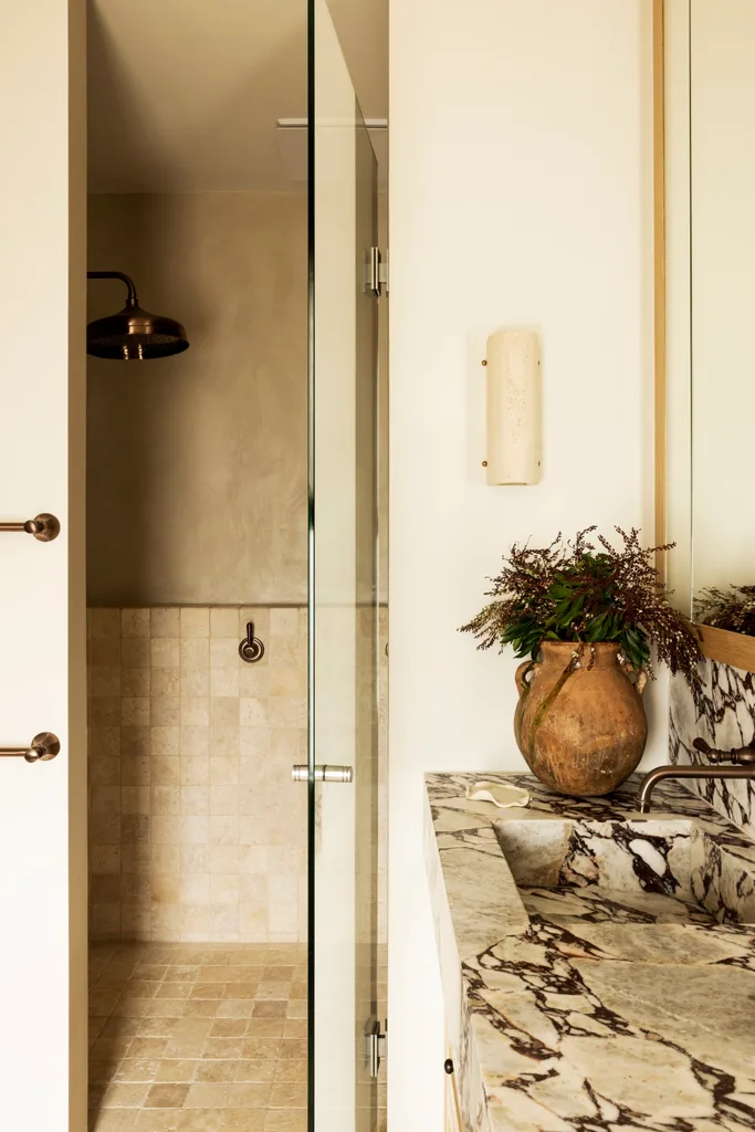 A bathroom with a brass showerhead, marble splashback and stone flooring.