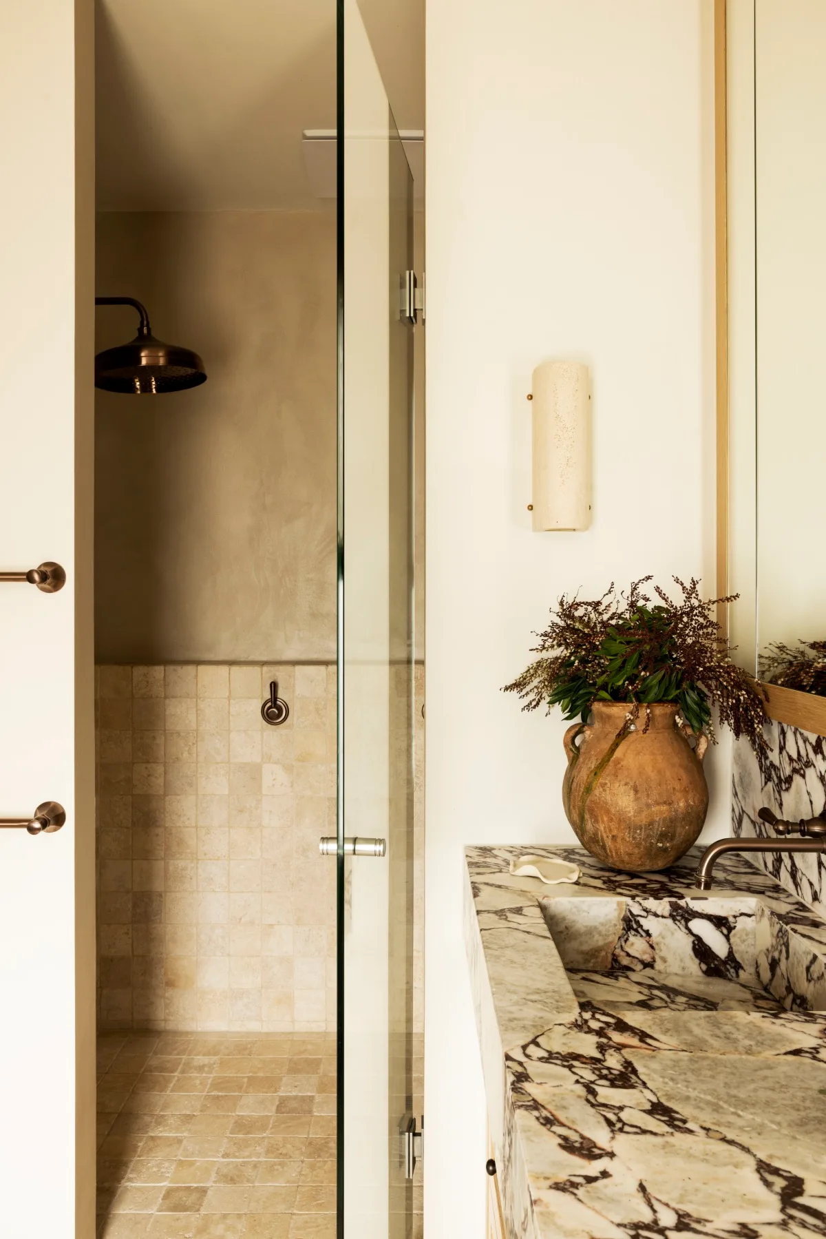 A bathroom with a brass showerhead, marble splashback and stone flooring. 