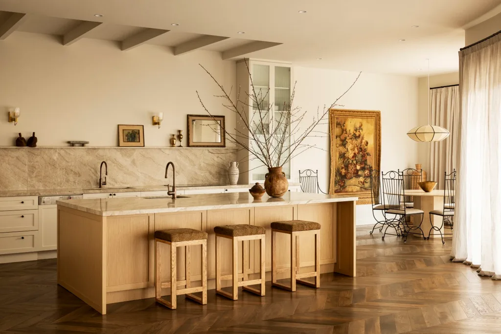 A warm-toned kitchen with a stone splashback and kitchen island, wood floors and soft curtains.