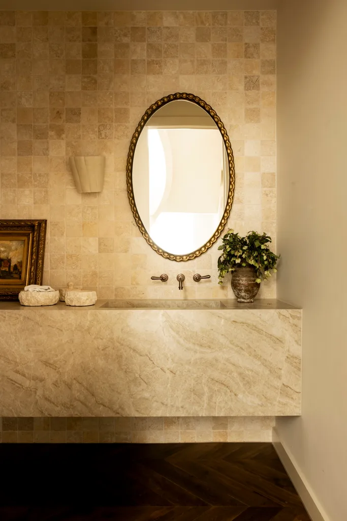 A stone powder room with a gold mirror.