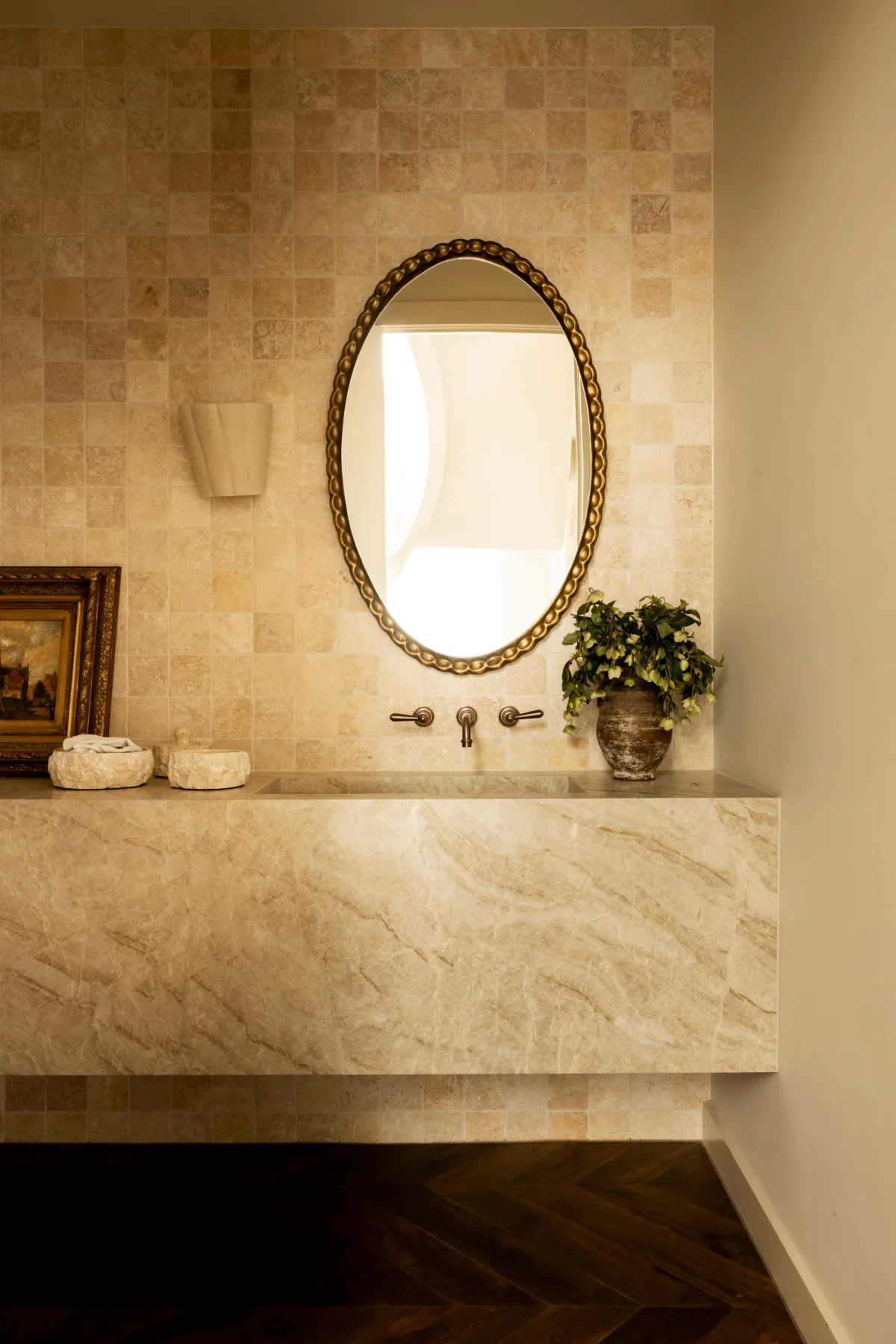 A stone powder room with a gold mirror. 