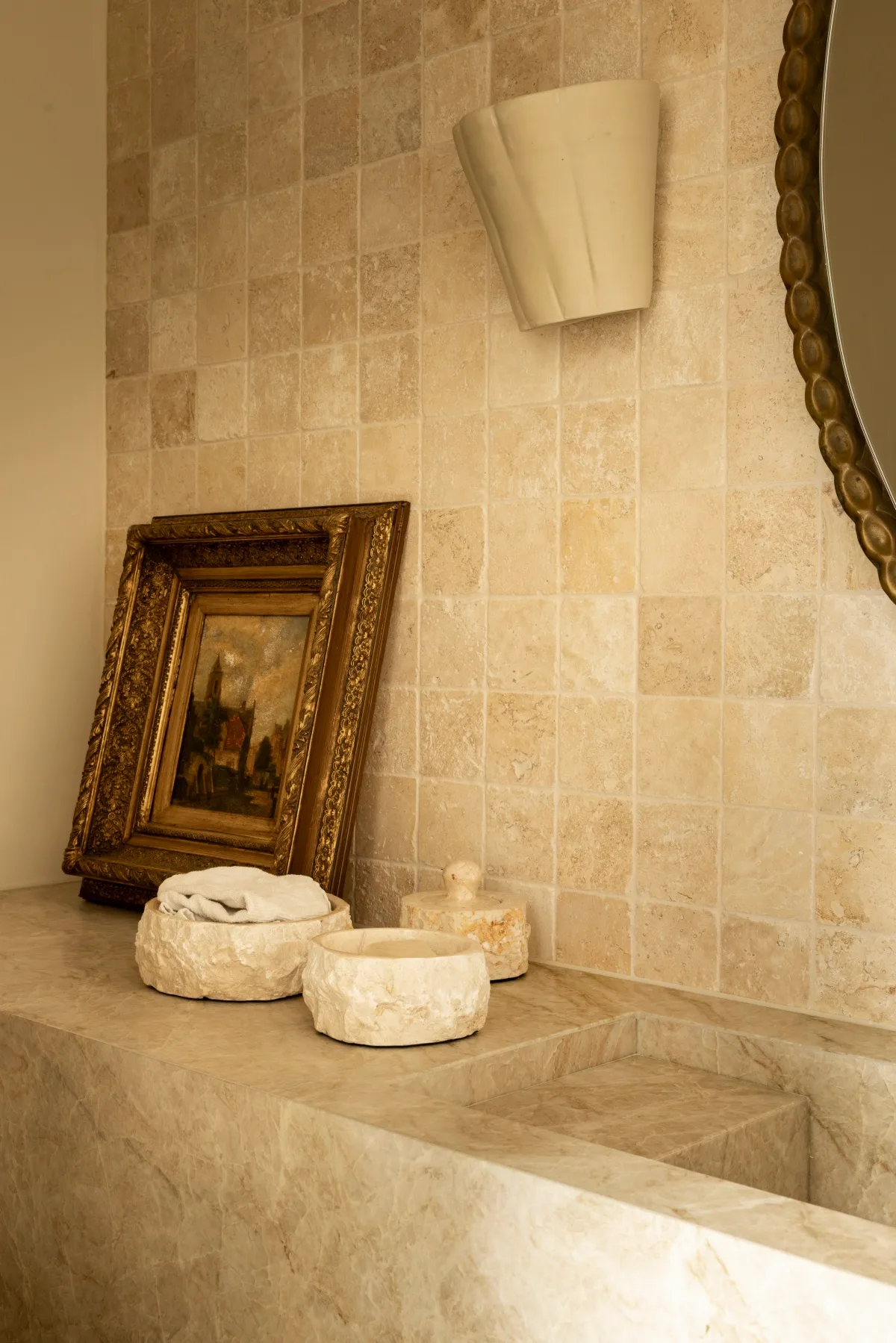 A stone splashback in a powder room with a vintage artwork and stone trays. 