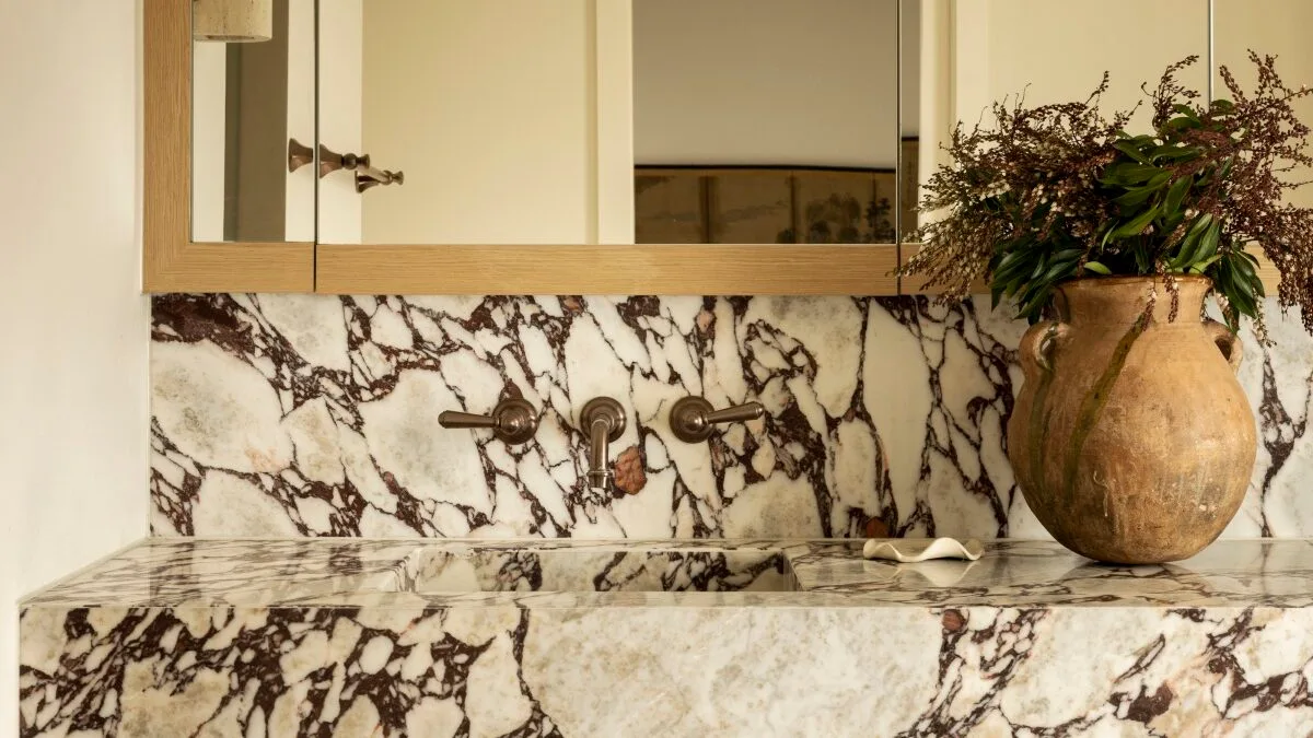 A bathroom with wood cabinetry and a marble splashback and benchtop.
