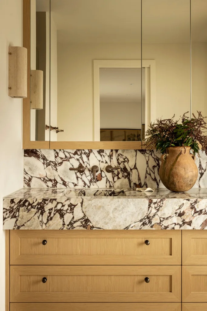 A bathroom with wood cabinetry and a marble splashback and benchtop.