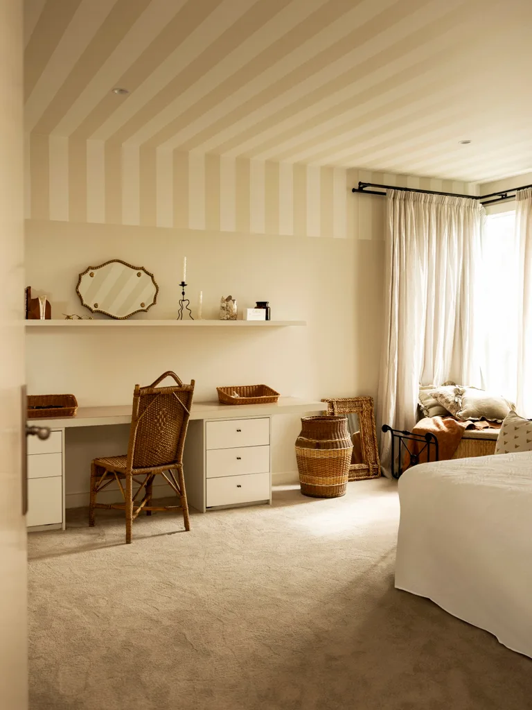 A bedroom with a dressing table, striped ceiling and rattan chair.