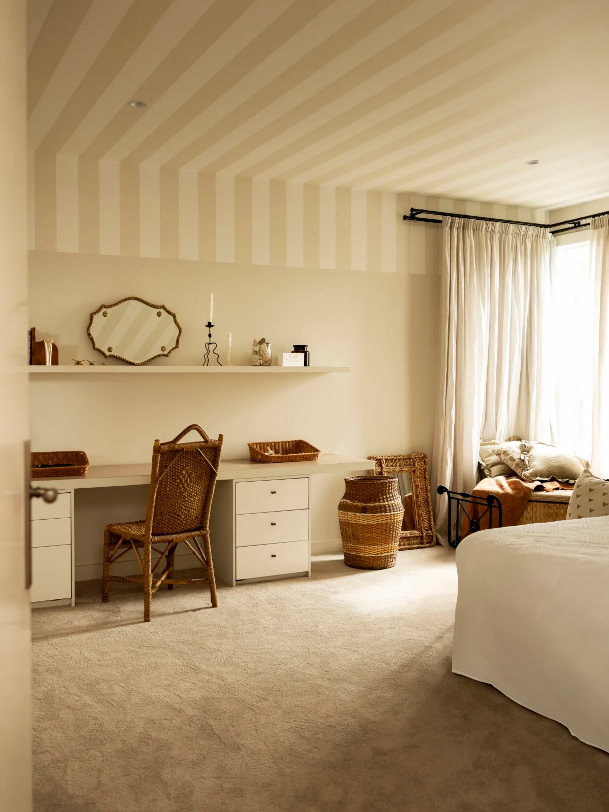 A bedroom with a dressing table, striped ceiling and rattan chair. 