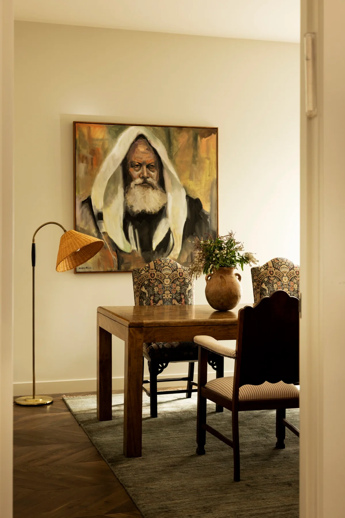 A dining room with a statement artwork, orange floor lamp and upholstered dining chairs. 