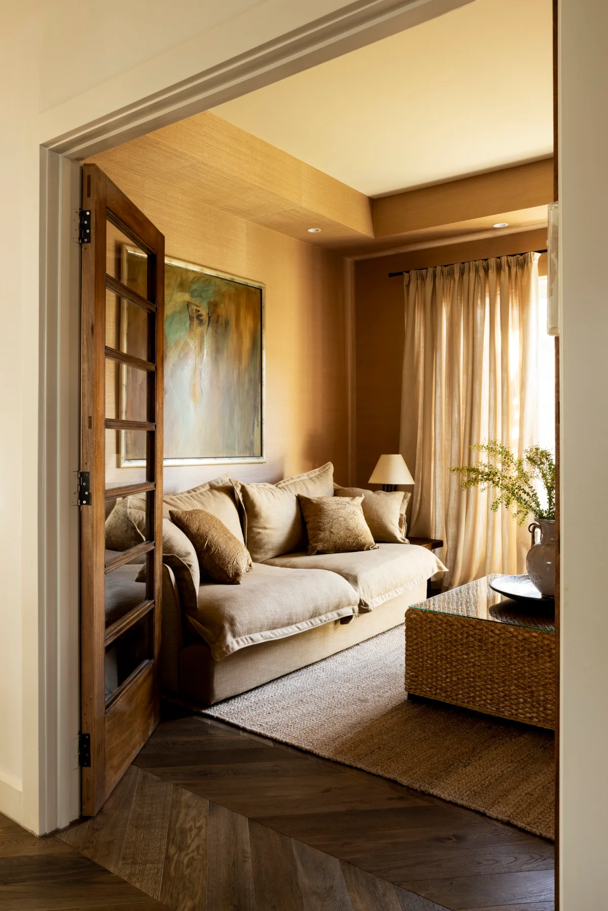 A honey coloured media room with a linen sofa, jute rug and rattan ottoman. 