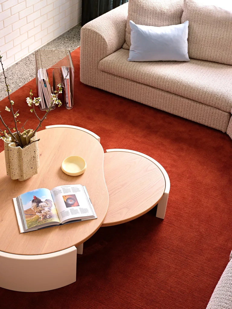 A close up of a grey sofa, timber coffee tables, all positioned on top of a bright red rug.