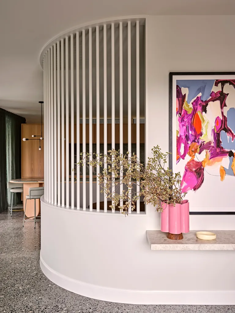 The entrance to a home, with a bright abstract painting on the wall, a pink vase overflowing with greenery and a marble shelf that the vase is positioned on. The kitchen is just visible around the corner. This was all part of an extension and renovation that lasted 13 months.
