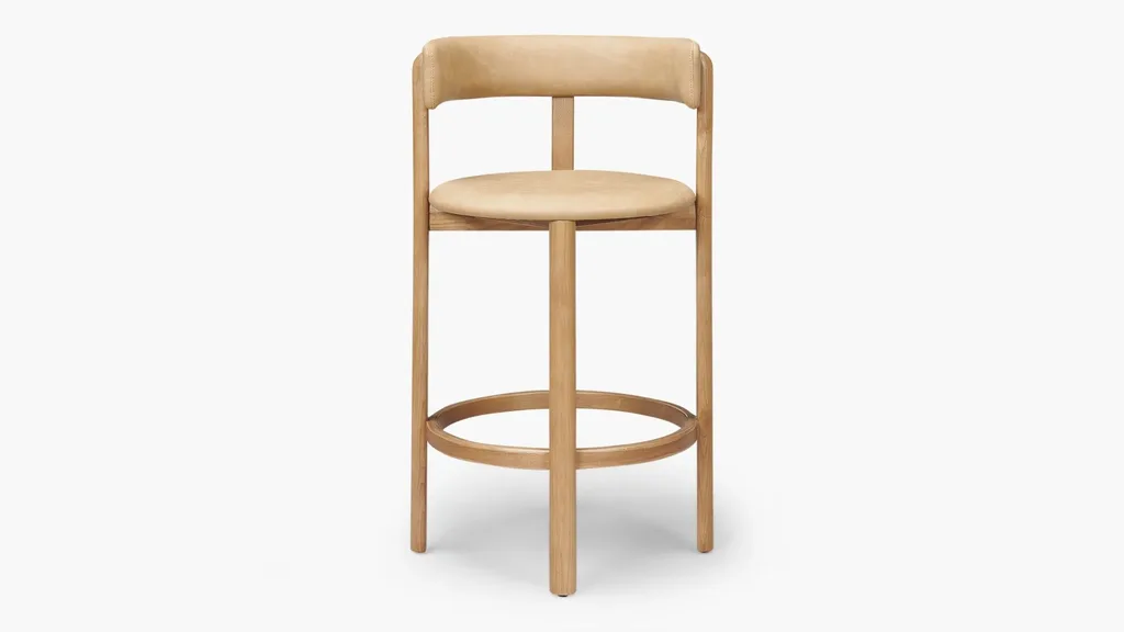 A bar stool with a round seat, curved leg rests, curved backrest and tan/caramel leather on the seats and backrest.