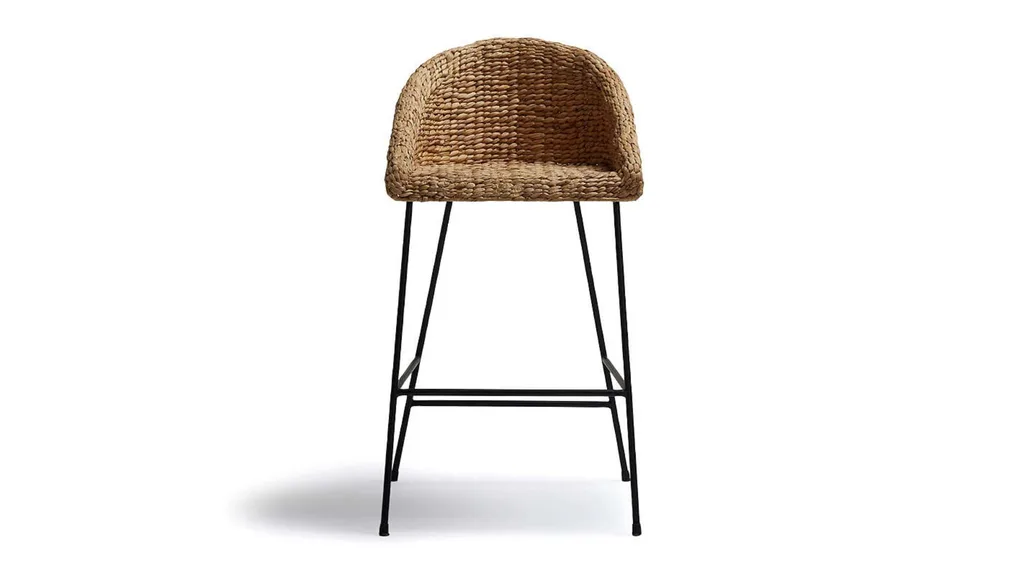 A bar stool with a black frame and leg rests and a woven, tactile seat and curved backrest.