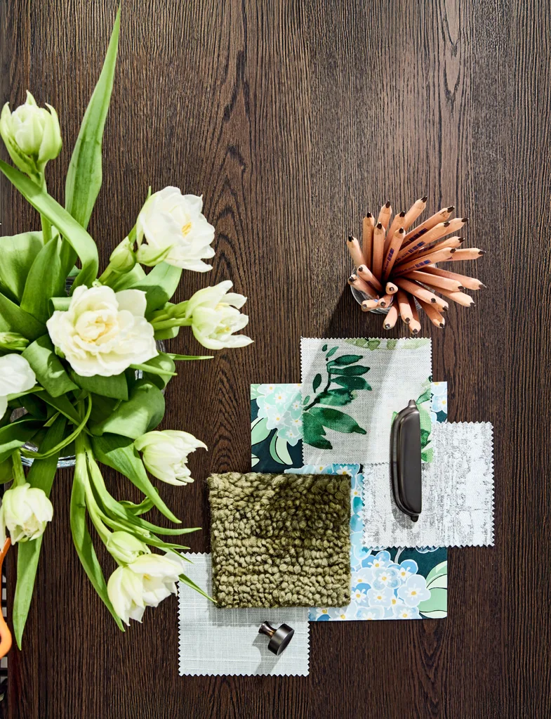 A timber background with fabric samples on top and a vase of white flowers beside.