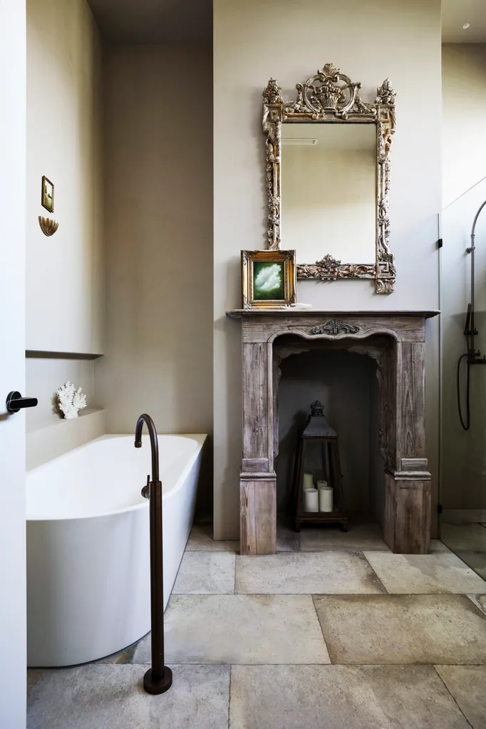 The main bathroom in Fleur Harris' home, which has large pavers on the floor, a wooden fireplace, an ornate frame and a large bath.