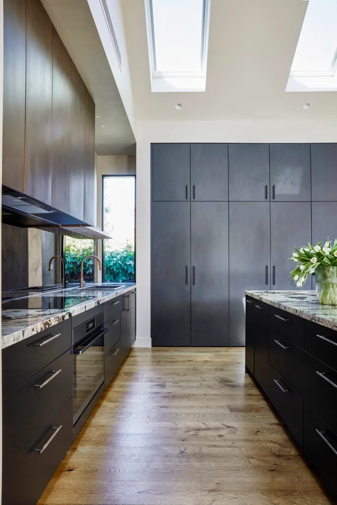 The kitchen in Fleur Harris' home features wall-to-ceiling black joinery and a brass splashback.