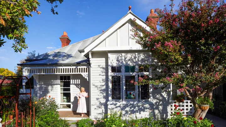 Fleur Harris stands on the deck of her heritage home, which has a thriving cottage garden out the front and a white picket fence.