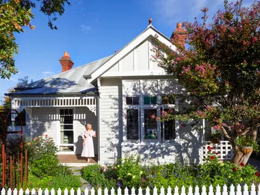 Fleur Harris stands on the deck of her heritage home, which has a thriving cottage garden out the front and a white picket fence.