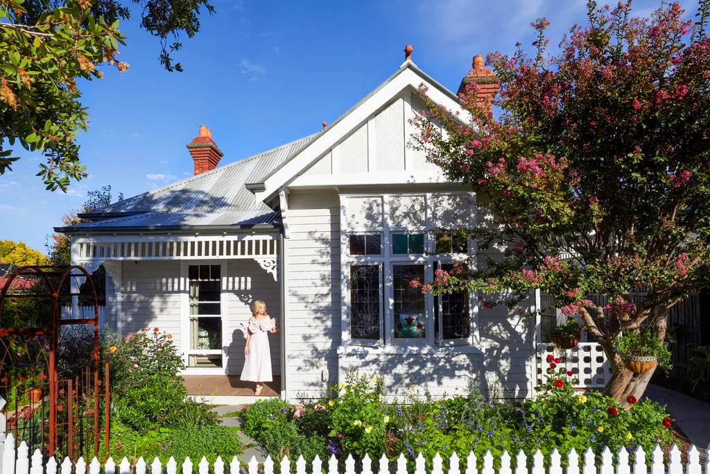 Fleur Harris stands on the deck of her heritage home, which has a thriving cottage garden out the front and a white picket fence.