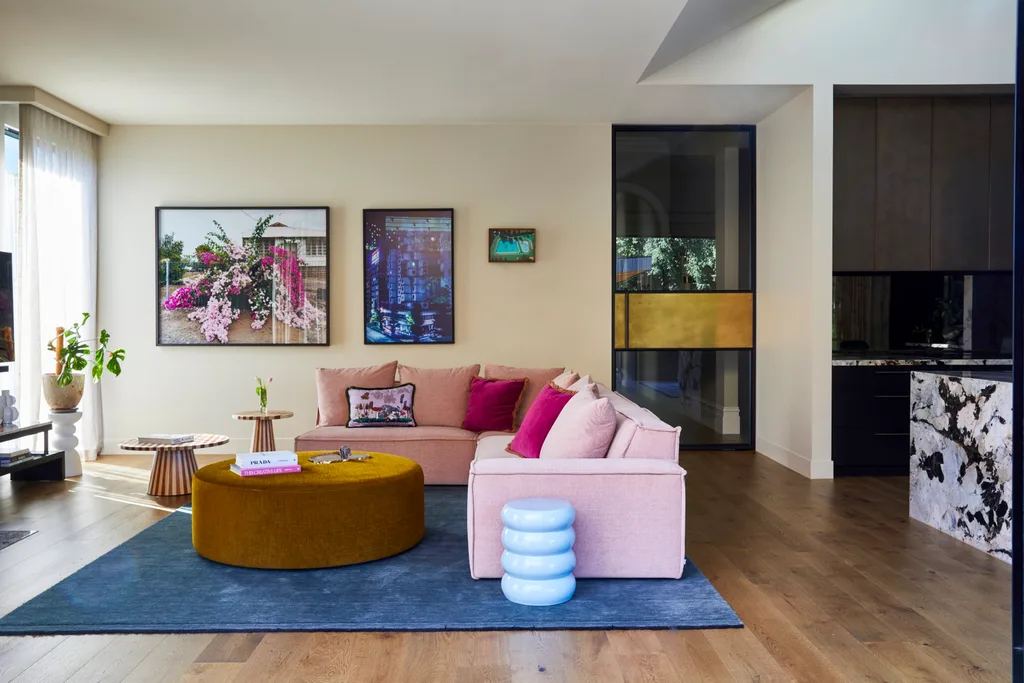 During her home renovation, Fleur Harris decorated her open plan living area with large artworks, a pink sofa, a blue rug and a mustard ottoman that serves as a coffee table due to its large size.