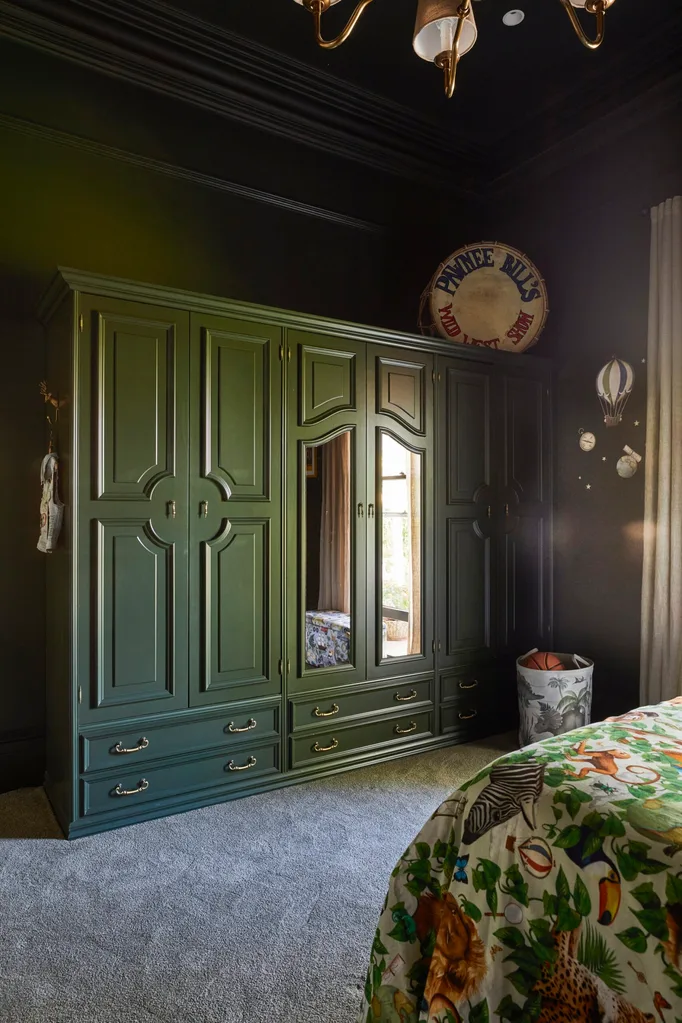 The bedroom of Fleur Harris' son, which has deep green walls and wardrobe, a green bedspread with African animals decorating it and wall decal stickers in the shape of hot air balloons.