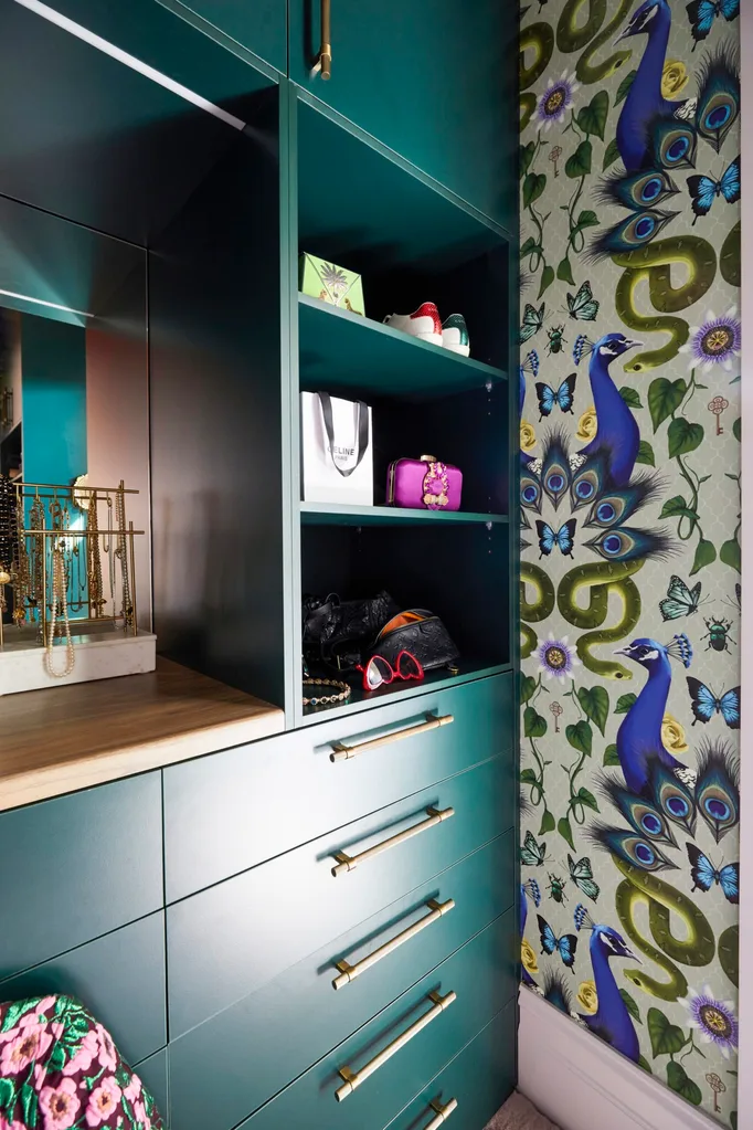 A close up shot of Fleur Harris' walk-in-robe, with a deep teal joinery, brass handles and wallpaper that is patterned with blue and green snakes, peacocks and butterflies.