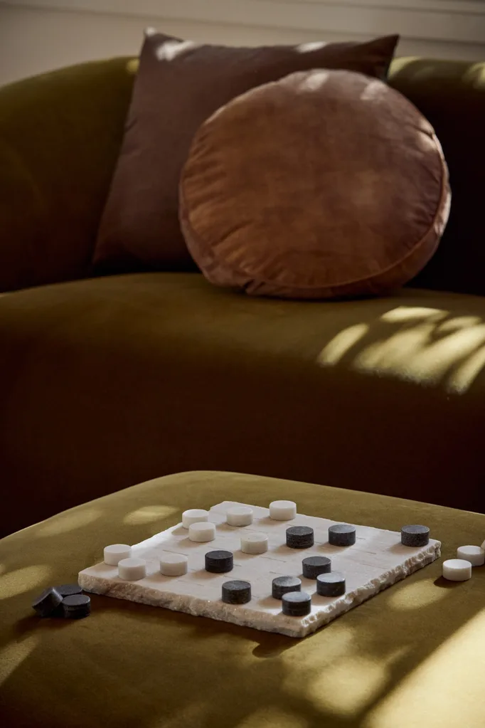 A green sofa that has been styled with a selection of cushions in deep, earthy tones. An ottoman is being used as a coffee table, complete with a board of checkers atop.