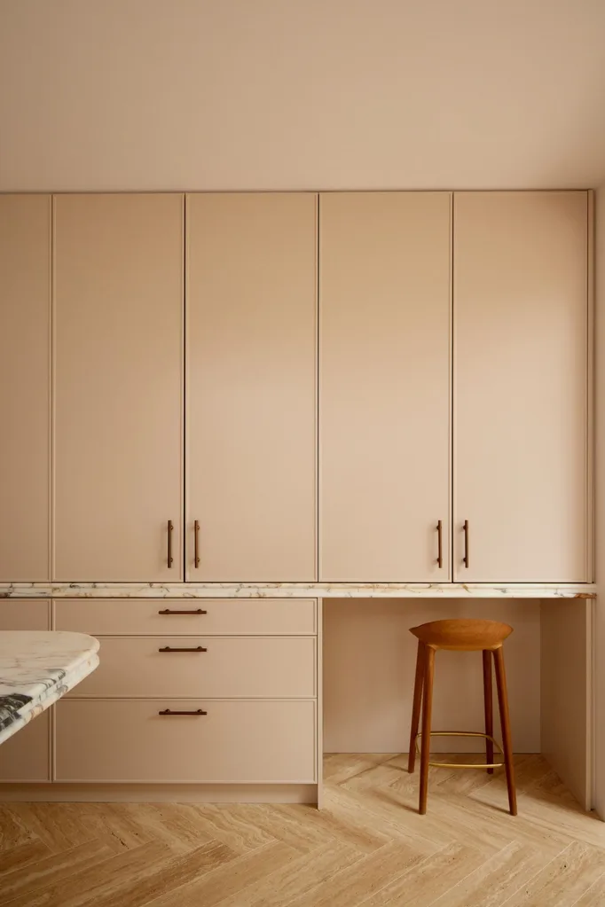 A kitchen with floor to ceiling cupboards. The cabinets are a dusty pink shade with brass pull handles.