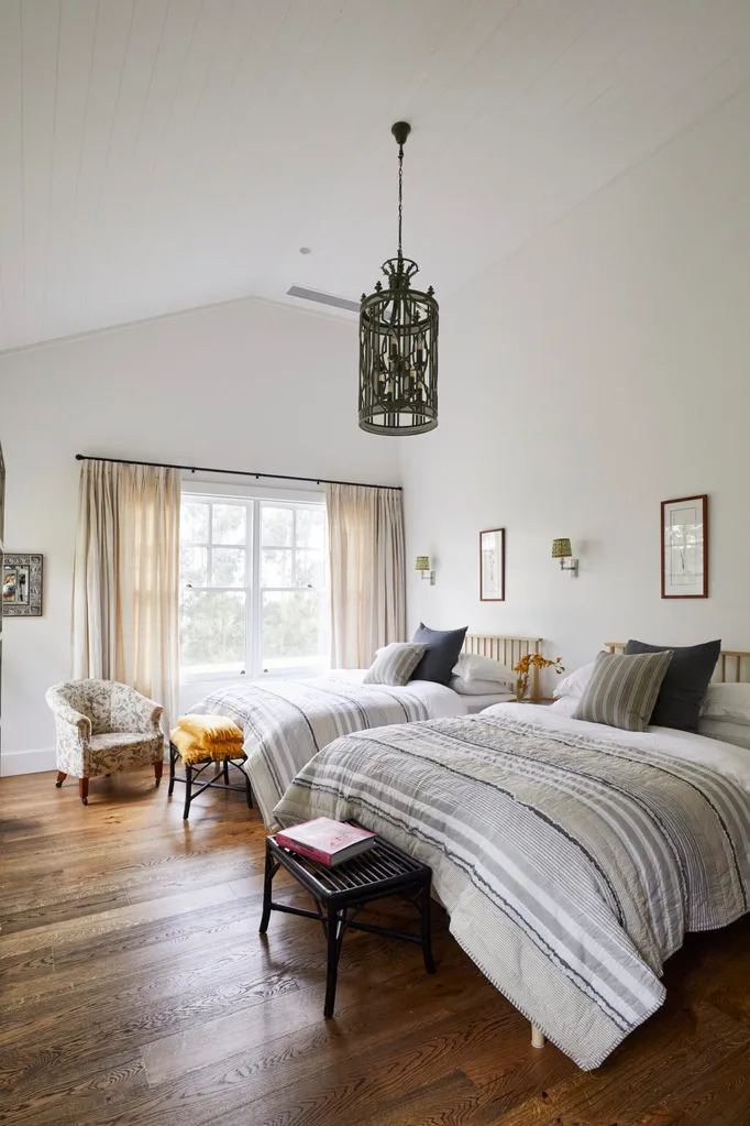 A modern farmhouse bedroom with two beds and a statement ceiling light.