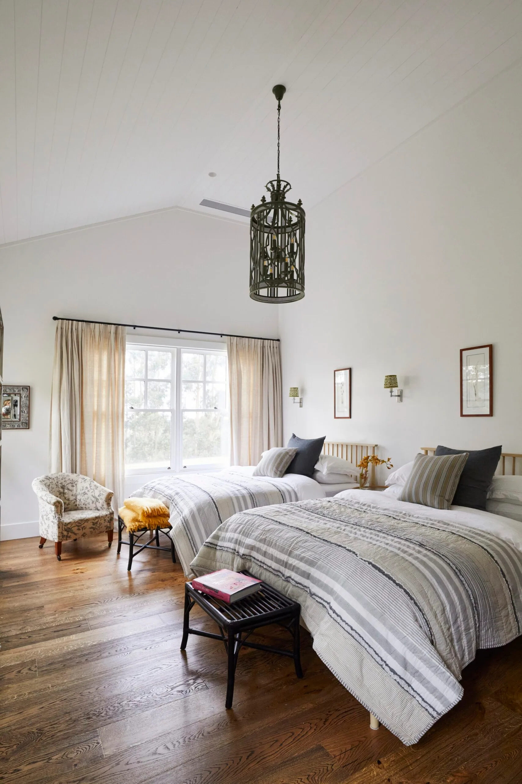 A modern farmhouse bedroom with two beds and a statement ceiling light. 