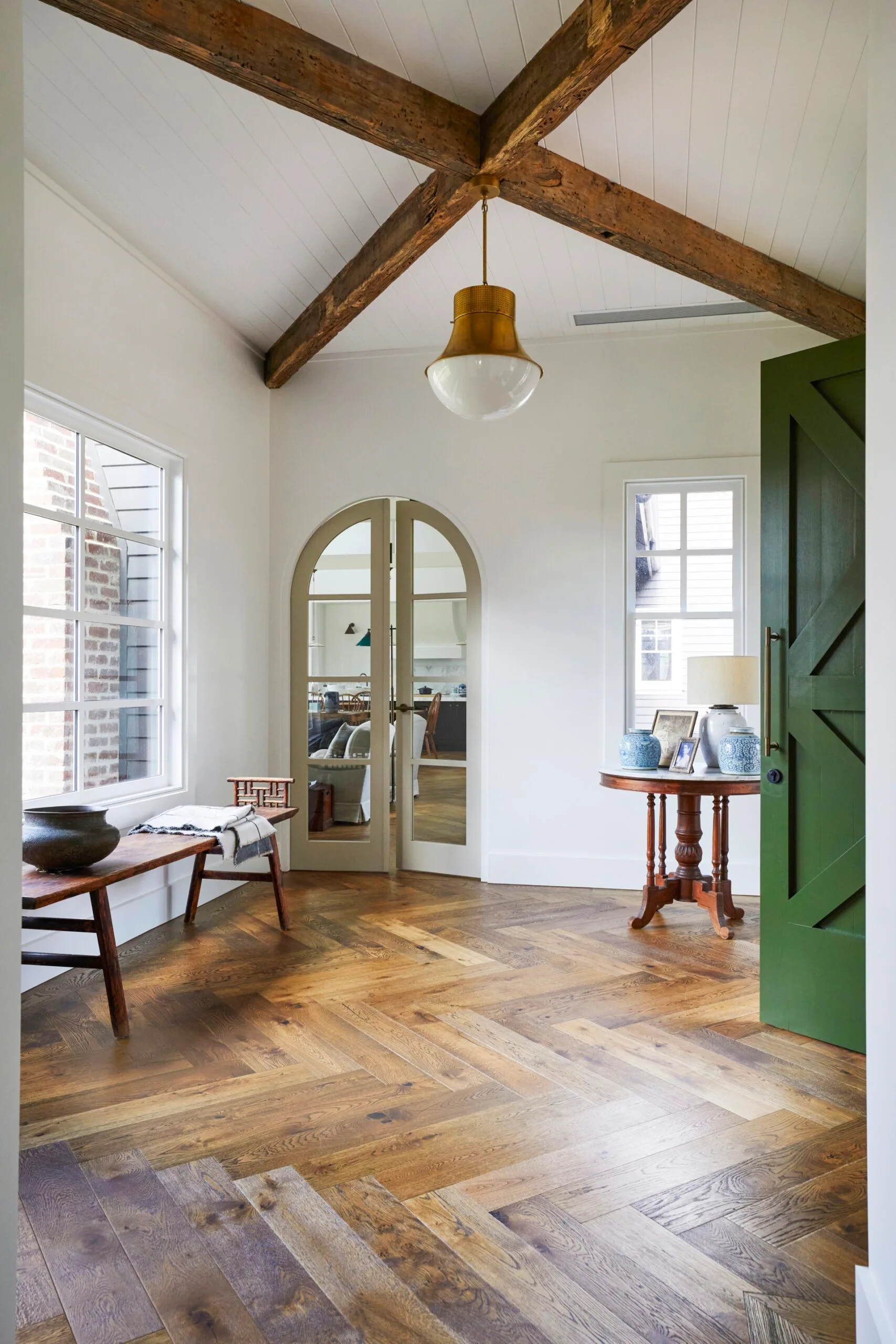 The entryway to a modern farmhouse with wood floors and a green french door. 