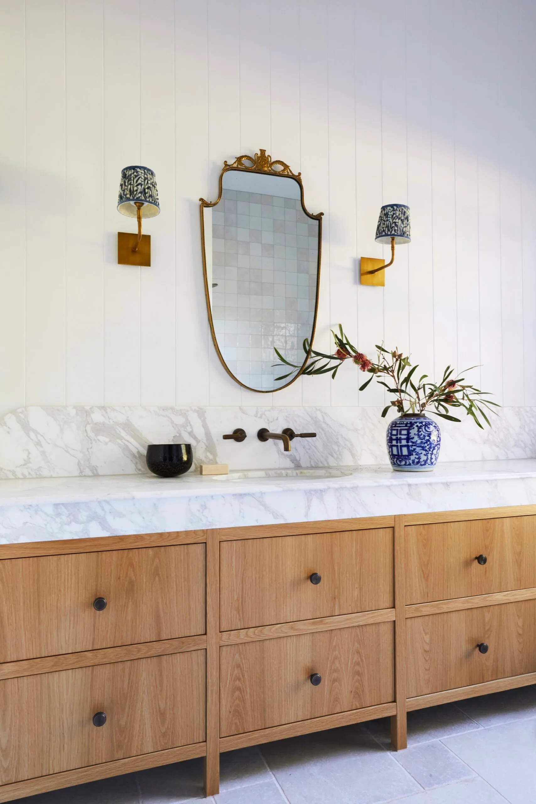 The timber cabinetry, wall sconces and statement mirror inside a modern farmhouse bathroom. 