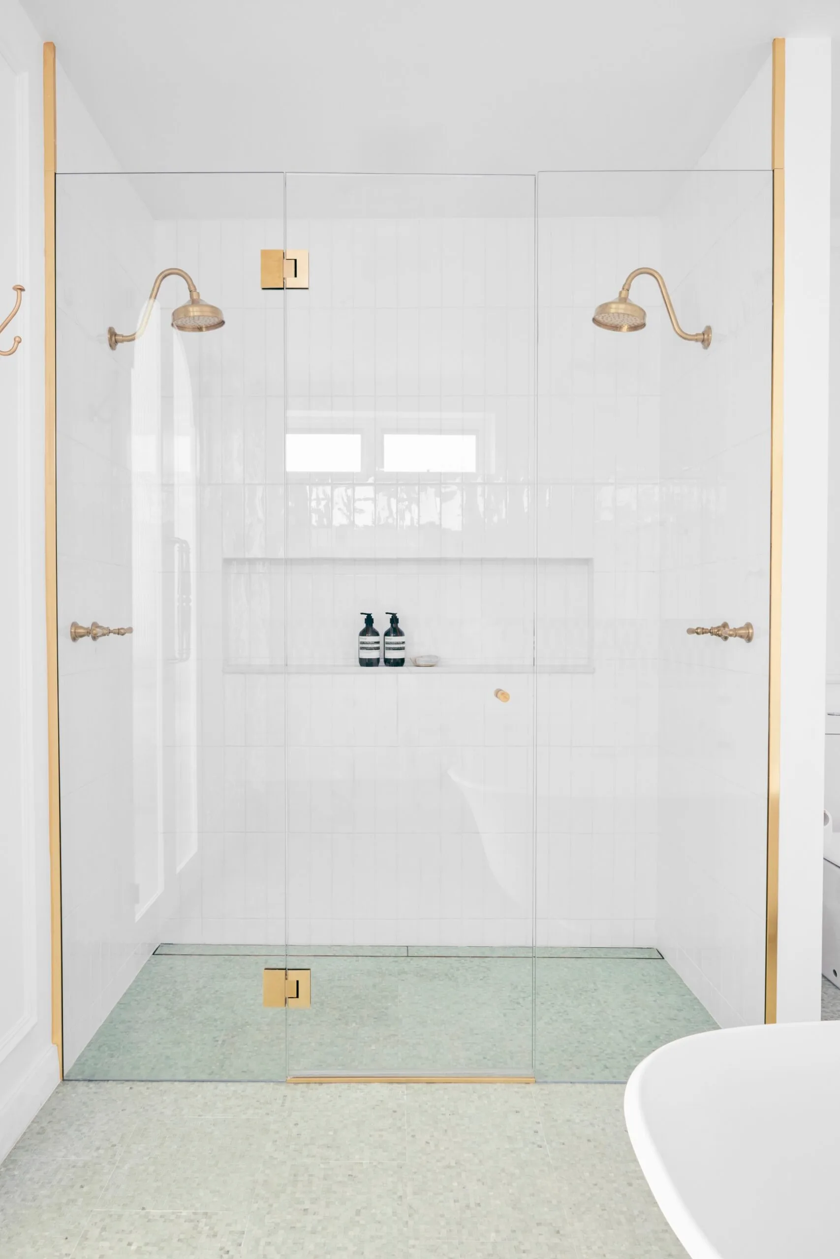 A luxurious double shower with a green mosiac tiled floor. 