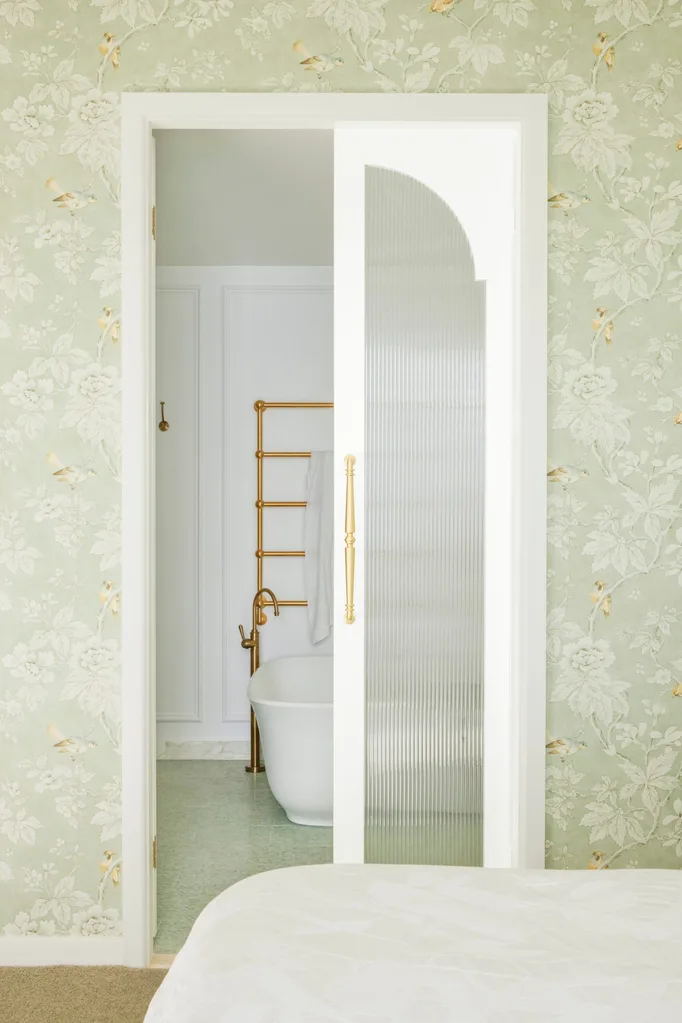 Green wallpaper and french doors leading through to a bathroom with a freestanding bath.