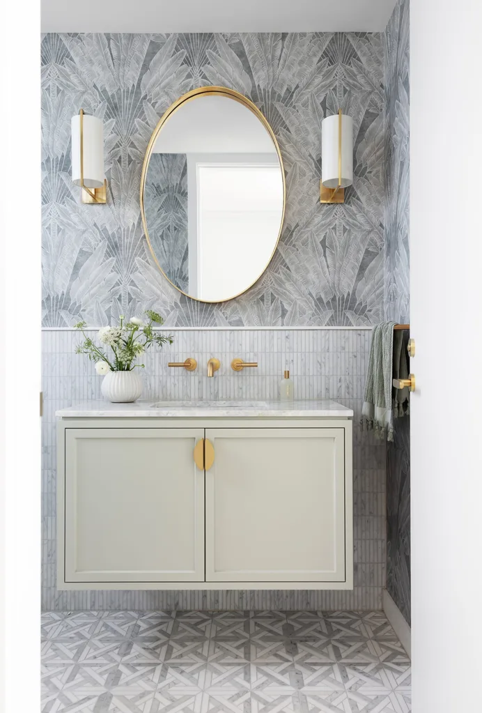 A powder room with wallpaper, wainscoting-style wall tiling, a basin built in to a vanity with joinery and a brass-framed mirror.